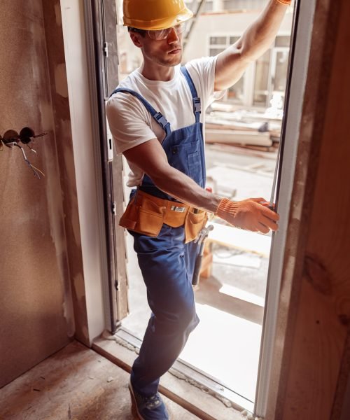 Handsome young man construction worker standing in doorway and using tape measure
